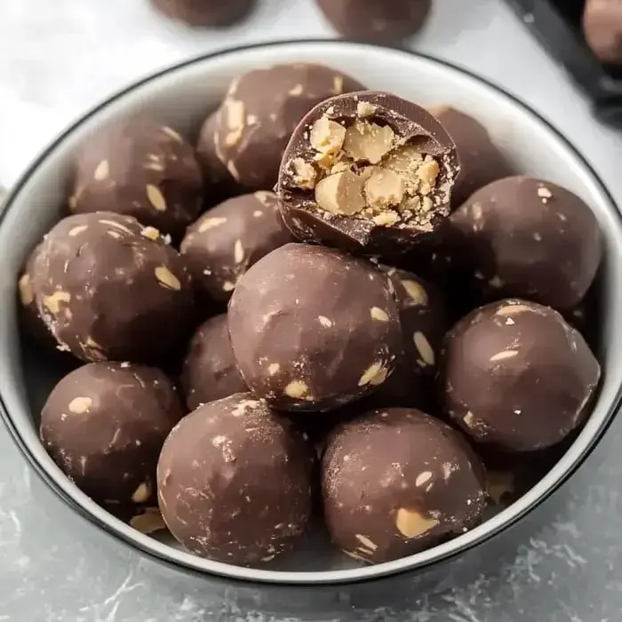 A bowl filled with chocolate-covered balls, one of which is cut in half to reveal a filling of nuts and oats.