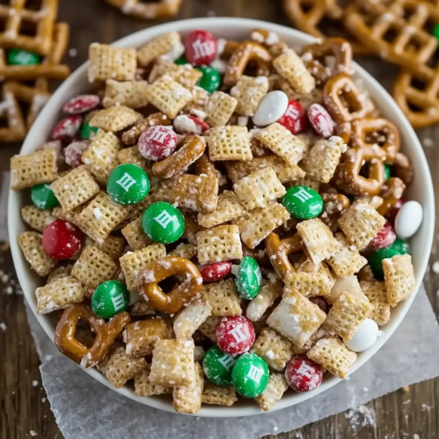 A bowl of festive snack mix containing cereals, pretzels, and colorful M&M candies.