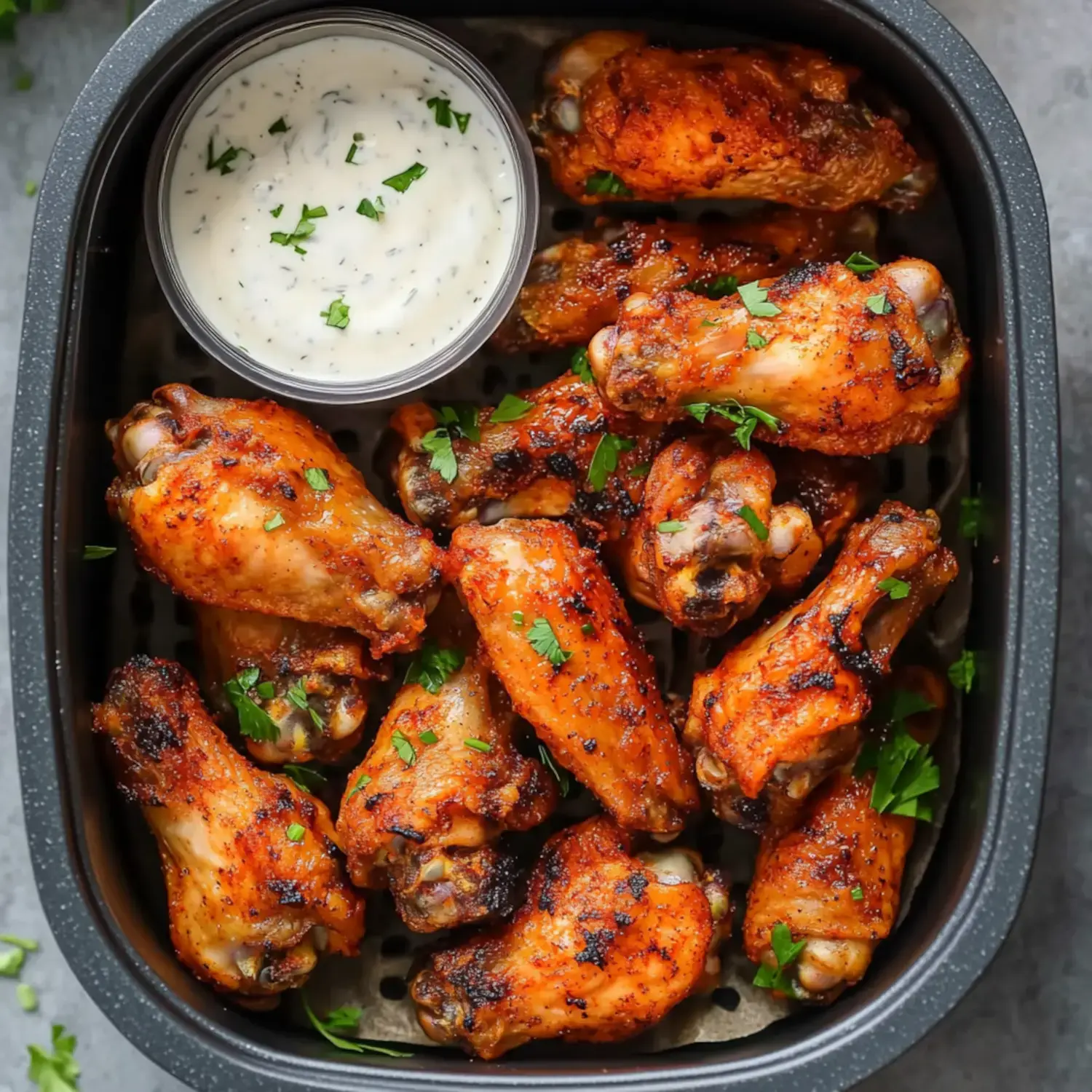 Golden brown chicken wings scattered on a serving plate with fresh parsley and a small dish of dipping sauce nearby.