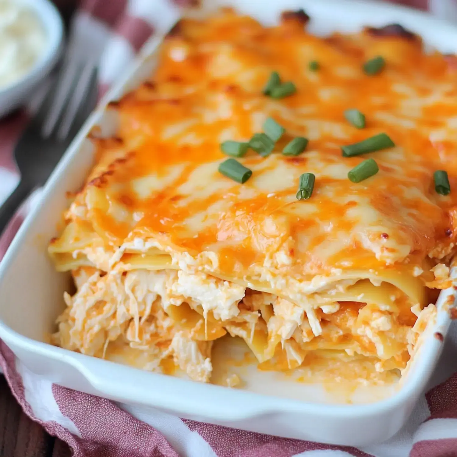 A creamy chicken lasagna, topped with melted cheese and garnished with chopped green onions, is served in a white baking dish.