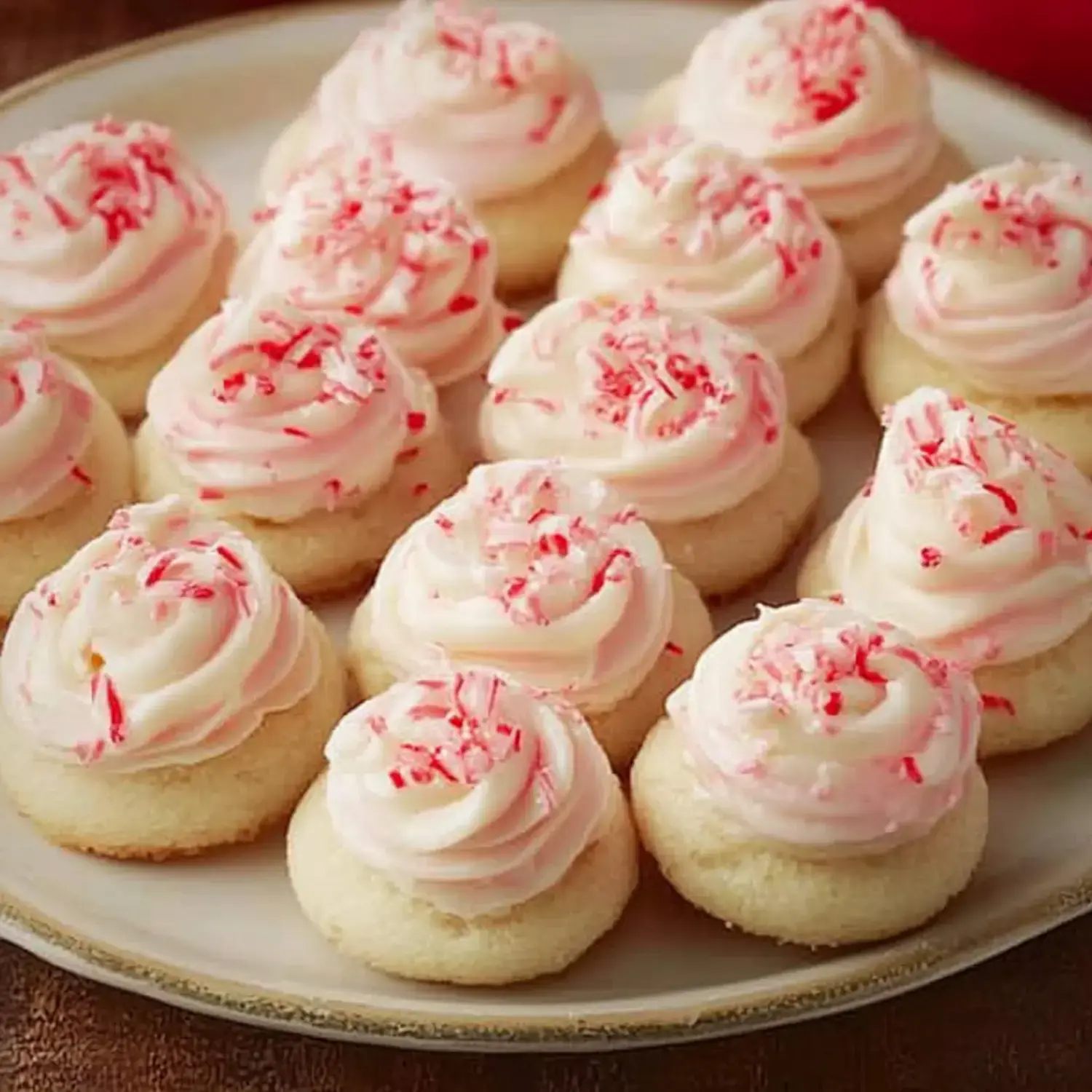 A plate of mini vanilla cupcakes topped with pink frosting and crushed peppermint.