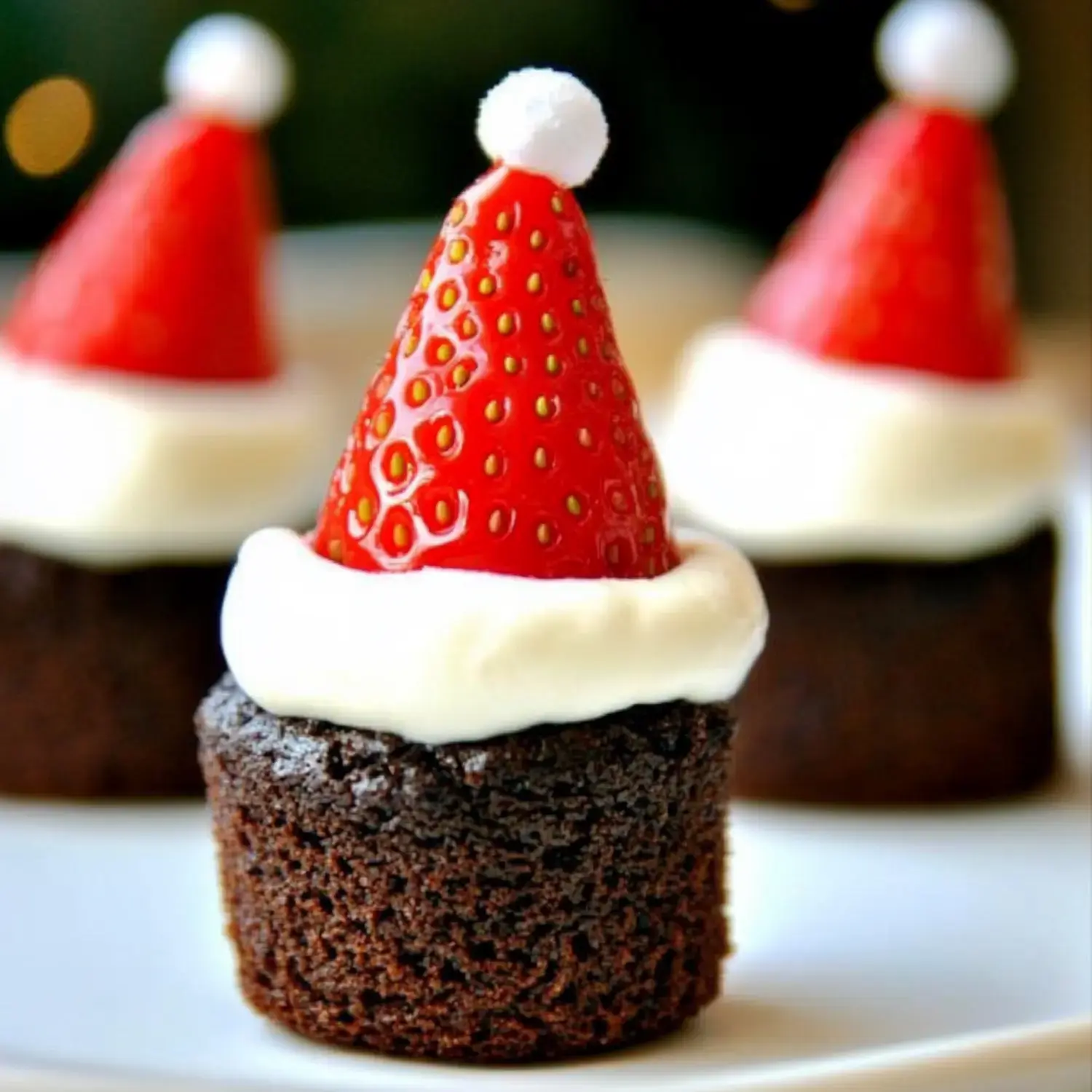 A close-up of chocolate cupcakes topped with white frosting and a strawberry shaped like a Christmas hat.